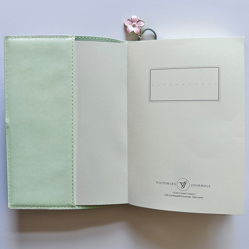 SAKURA journal for girls in stylish fashion colors, high-quality paper, compact and easy to carry, with elastic band and brass floral pendant. By Victoria's Journals.